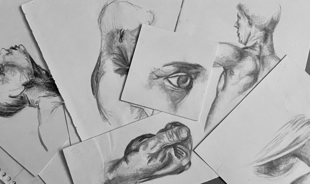 A handful of overlapping pages showing pencil sketches depicting human figure studies. There are images of an eye, a hand balled into a fist, and several busts with faces tilted in different directions.